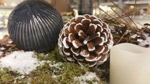 Graue Weihnachtskugel mit Tannenzapfen und Kerze auf Schnee-Moß-Dekoration
