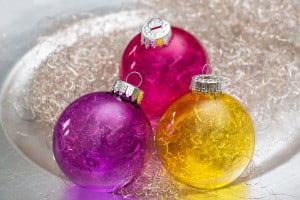 Drei Weihnachtskugeln mit leuchtenden Farben. Gelb, violett und pinke Kugeln.